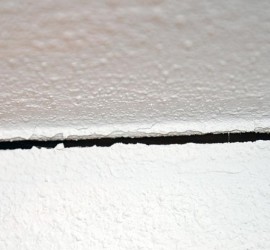 Riss im Flur am Übergang Wand-Decke, Zeigefinger zum Größenvergleich